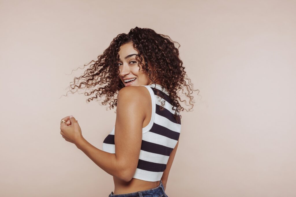Cheerful brunette woman moving long curly hair